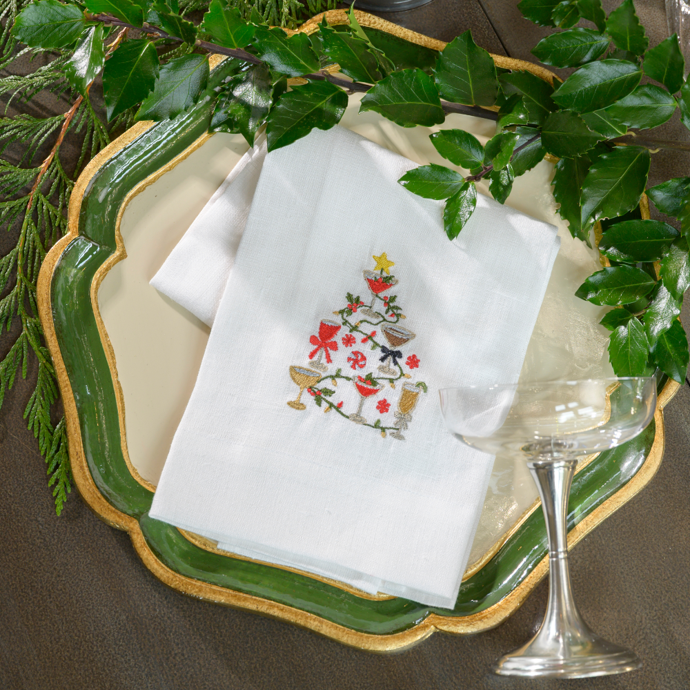 Christmas Cocktails embroidered on a white linen towel in the shape of a tree on a tray with greens and a Verona Champagne coupe