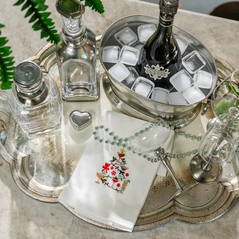 A bar set up with pewter and glass stemware and decanters with champagne in a wine bucket and a folded Christmas cocktails linen towel folded