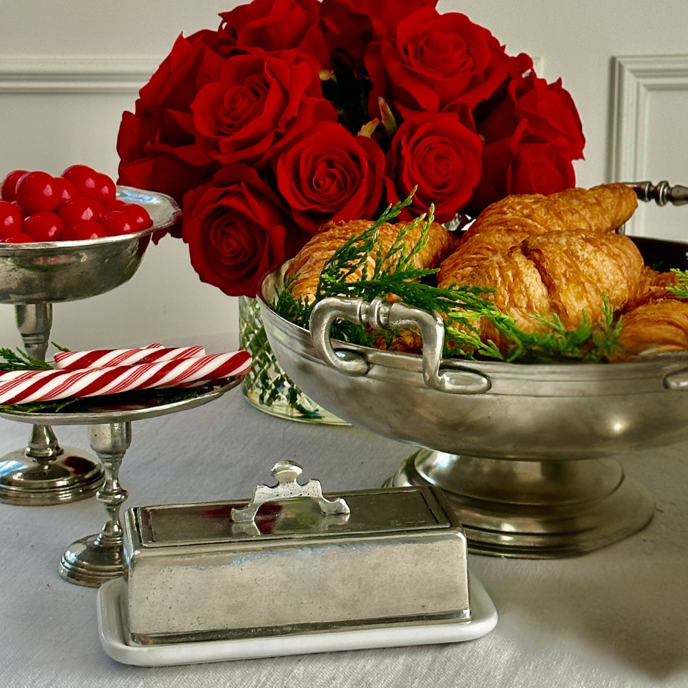 Silver platter with croissants, red roses, and a butter dish on a table.