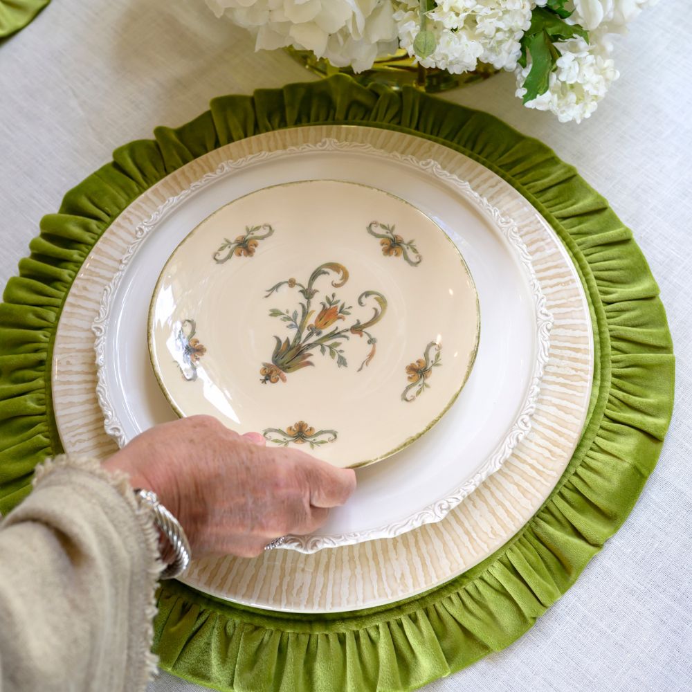 Decorative Cream Striped charger plate with Italian floral design on a green placemat, held by a hand.