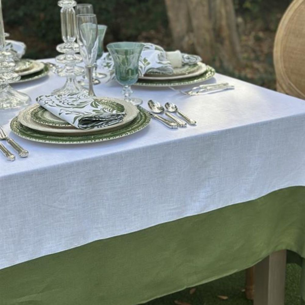 Dining table set with green and white linen tablecloth, Firenze plates, cutlery, and glasses outdoors.