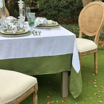 Dining table set with evergreen and white linen tablecloth, chairs, and decorative items outdoors.