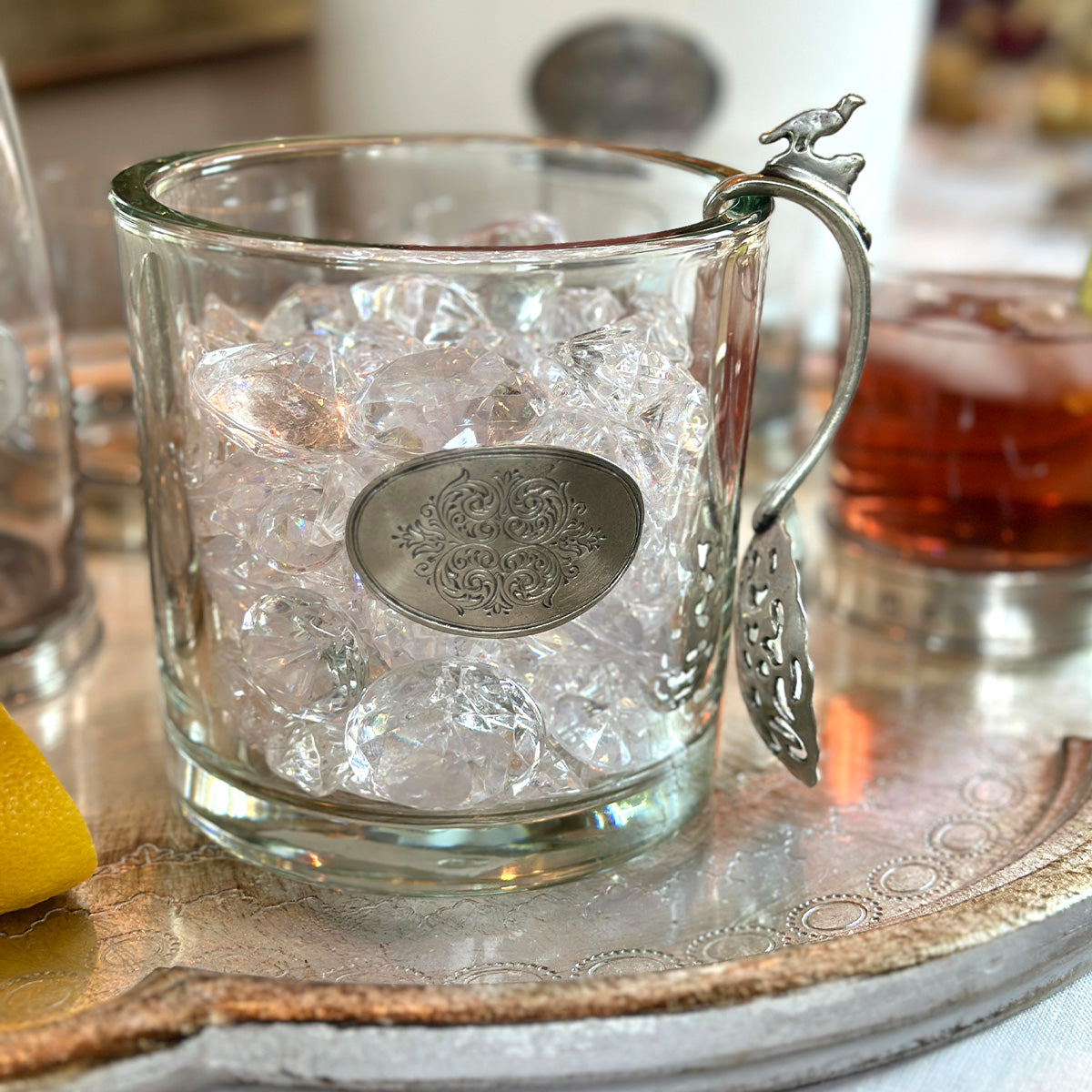 Arte Italica Damasco glass vessel filled with ice, styled as an ice bucket with ornate pewter handle on silver tray