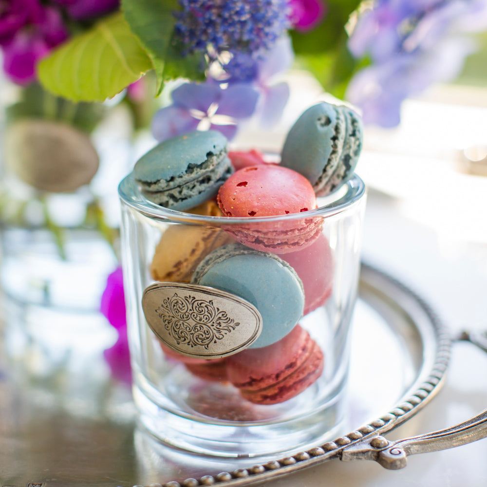 Arte Italica Damasco glass vessel filled with pastel French macarons on a silver tray with purple florals