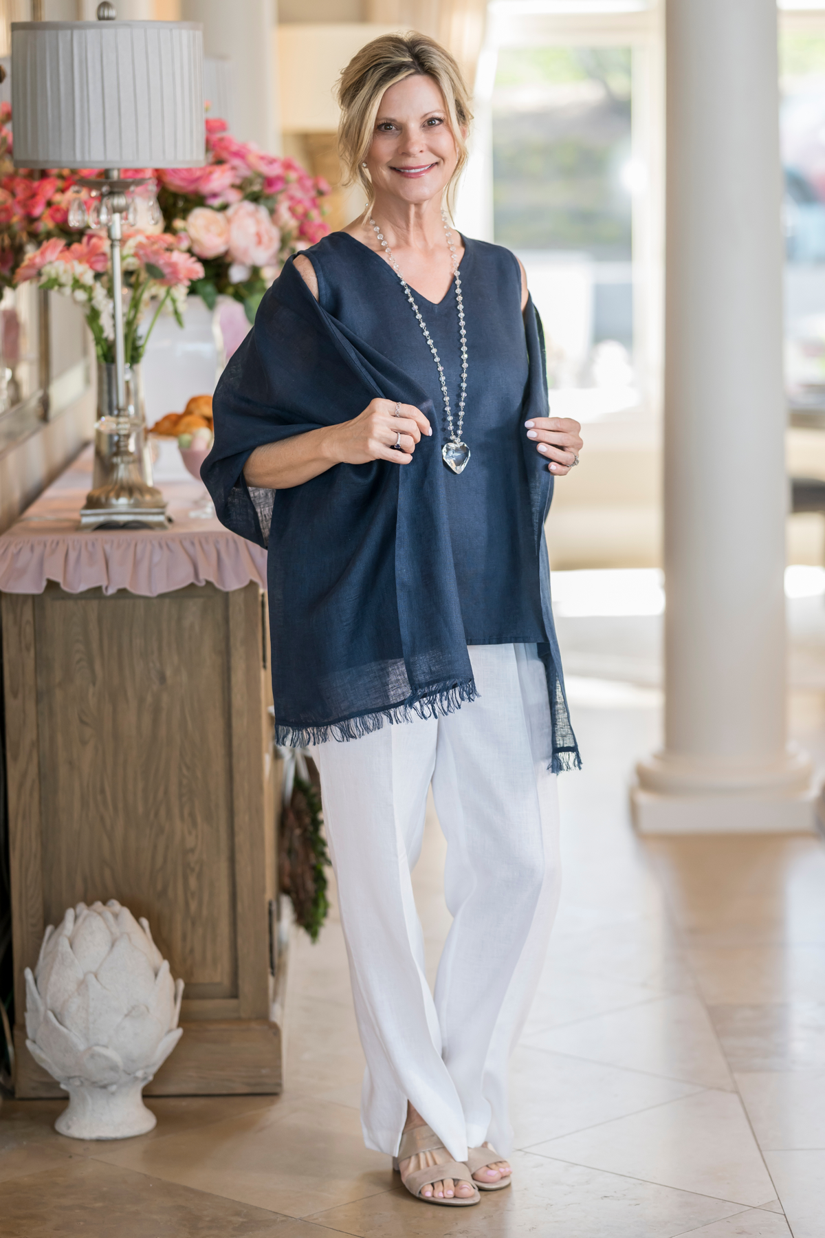 Woman wearing navy Farrah Fringe linen scarf draped as a shoulder wrap over white linen pants. --Arte Italica and Crown Linen Designs