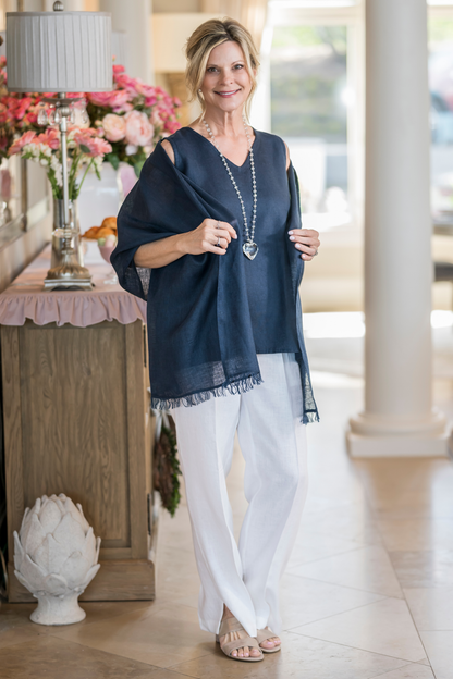 Woman wearing navy Farrah Fringe linen scarf draped as a shoulder wrap over white linen pants. --Arte Italica and Crown Linen Designs