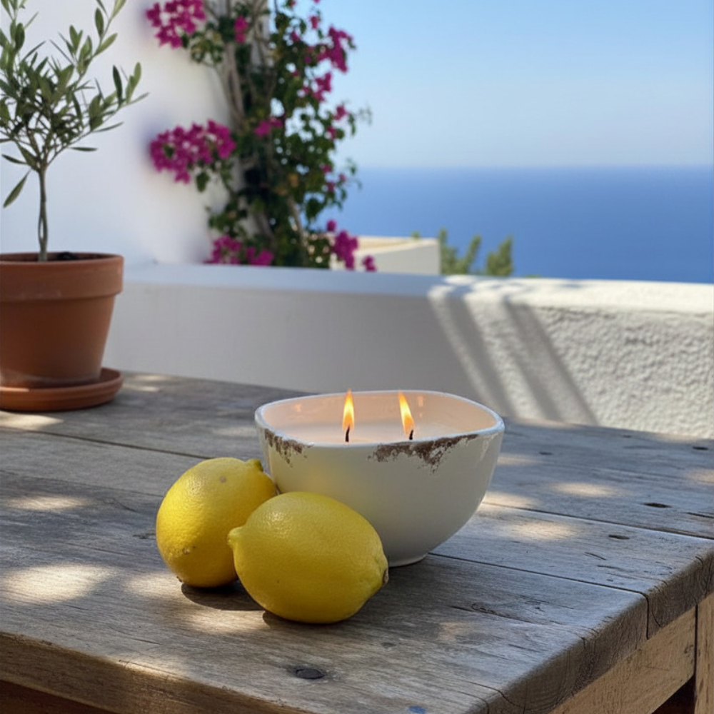 Candle in a white bowl with two lemons on a wooden table, with a scenic background.