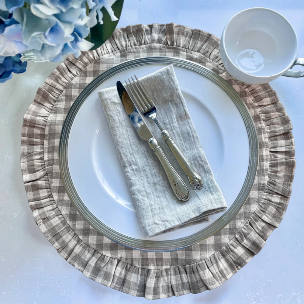 Plated dinner setting with checkered linen ruffle placemat, white plate, silverware, and napkin on a light blue background.