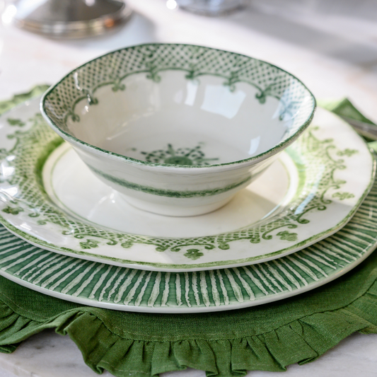 A set of ceramic tableware with green and white patterns, including a cereal bowl and a dinner plate, placed on a green cloth on a table.