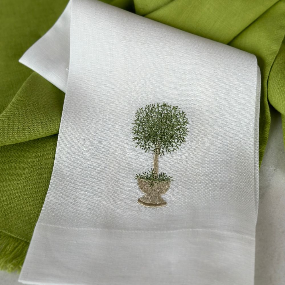 White linen towel with embroidered herb topiary design on a green fabric background