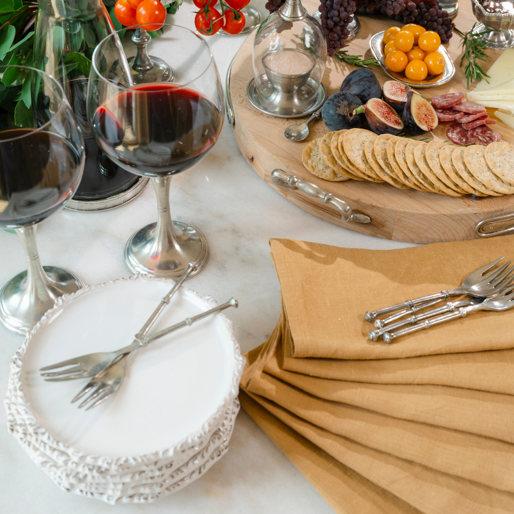 A charcuterie spread on a table with wine and a cheese board with stacked Imperial bread canape plates