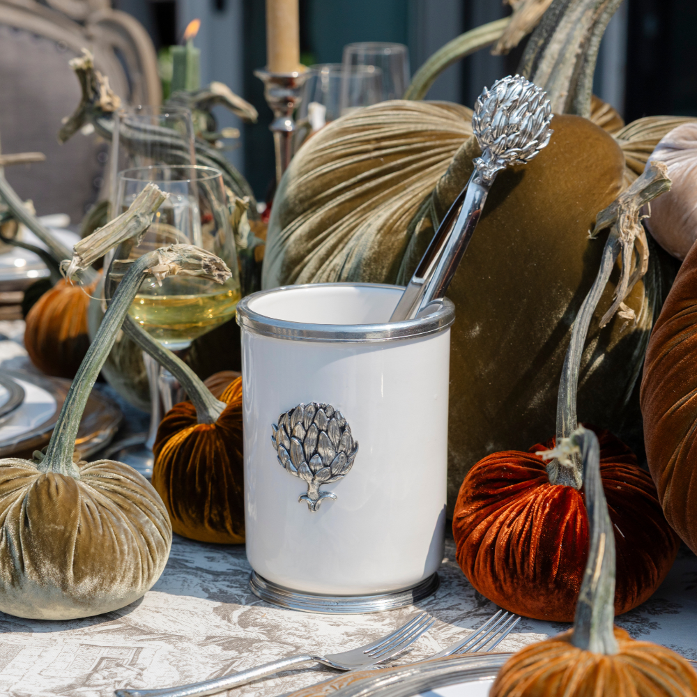 Italian Tuscan Ceramic Vessel with Pewter Artichoke Emblem with Artichoke tongs in it sittings on a Fall table with velvet pumpkins and wine glasses