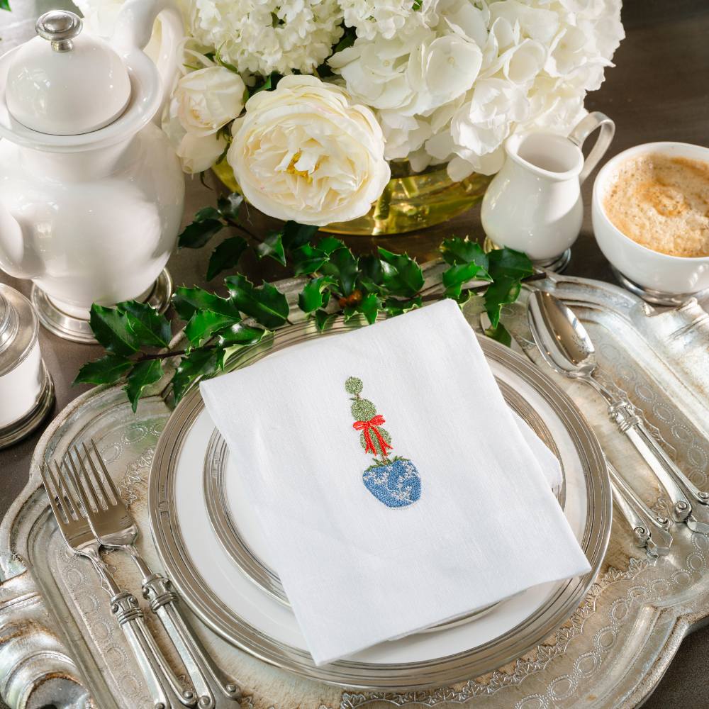 A white linen towel embroidered with a green, red and blue La Jardin Triple topiary design on Tuscan plates