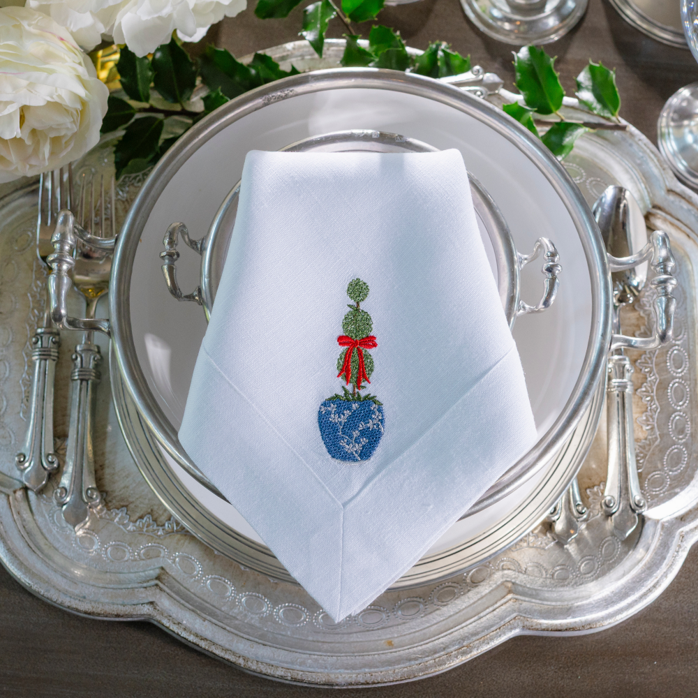 A Florentino silver tray with Tuscan plate and a folded large white linen napkin embroidered with a topiary that has a blue pot and red bow