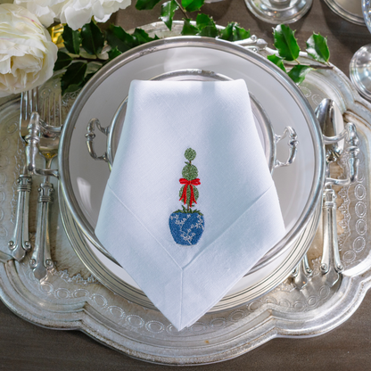 A Florentino silver tray with Tuscan plate and a folded large white linen napkin embroidered with a topiary that has a blue pot and red bow