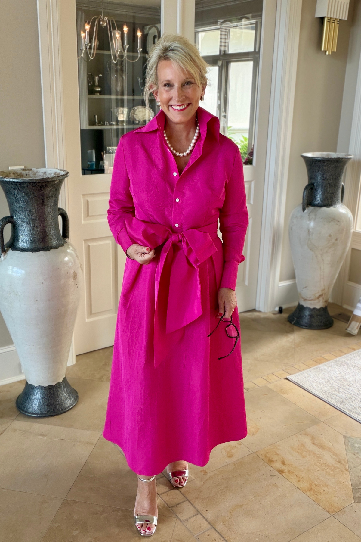 Large fuchsia taffeta sash tied in a bow at the waist over a fuchsia Candace blouse and matching Lizzy skirt, styled with a pearl necklace and heels in an elegant foyer