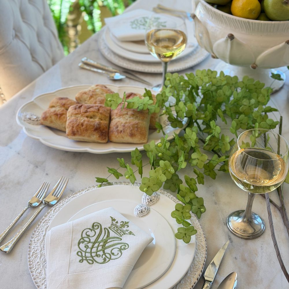 Table set with Leone dinnerware with green flowers and a platter with rolls and wine glasses on the table