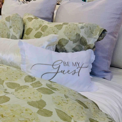 Floral bedding with a pillow that says 'Be My Guest' on a bed.