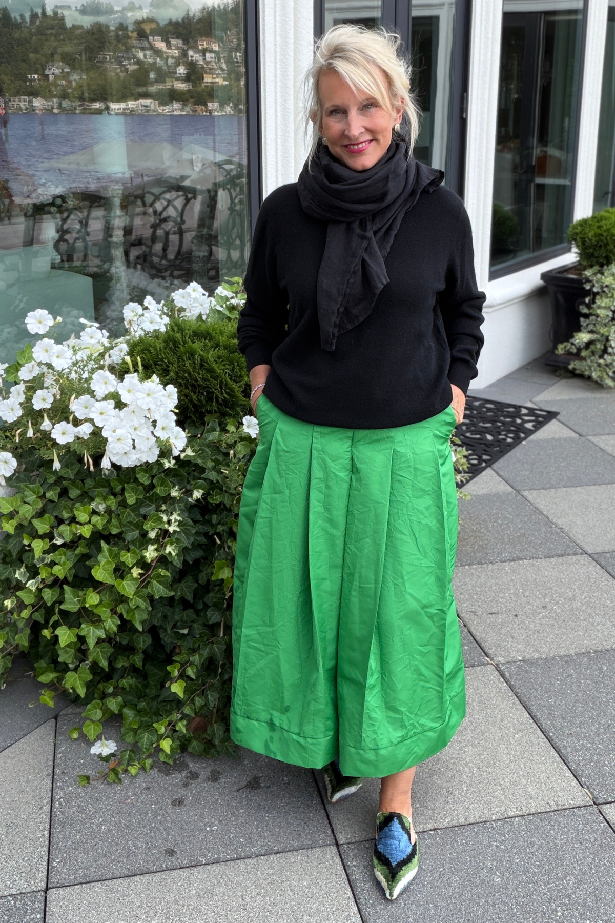 Black linen Stevie scarf loosely wrapped around the neck, styled with a black sweater and emerald green Lizzy taffeta skirt outdoors