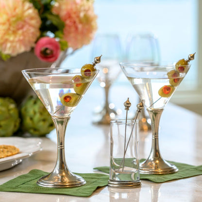 Two Verona martini glasses with Crown Picks as olive skewers on a table with flowers in the background