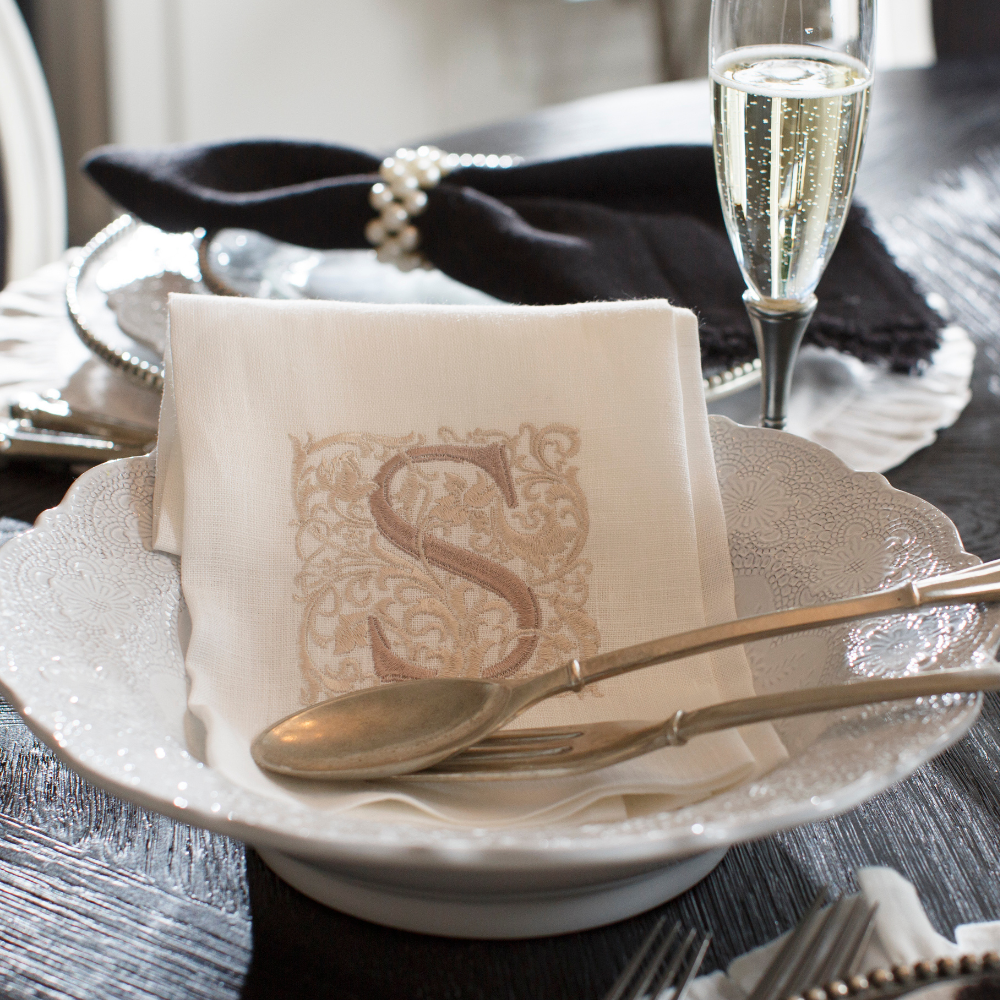 A Merletto antique white serving bowl on a table with Peltro salad servers and a white linen Monogram S towel in it