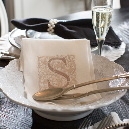 A Merletto antique white serving bowl on a table with Peltro salad servers and a white linen Monogram S towel in it