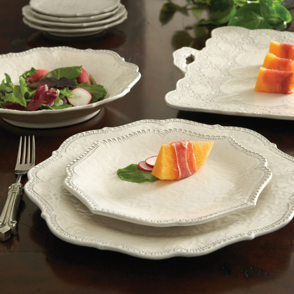 Merletto Antique White salad plate stacked on a dinner plate with a salad and appetizer on a table