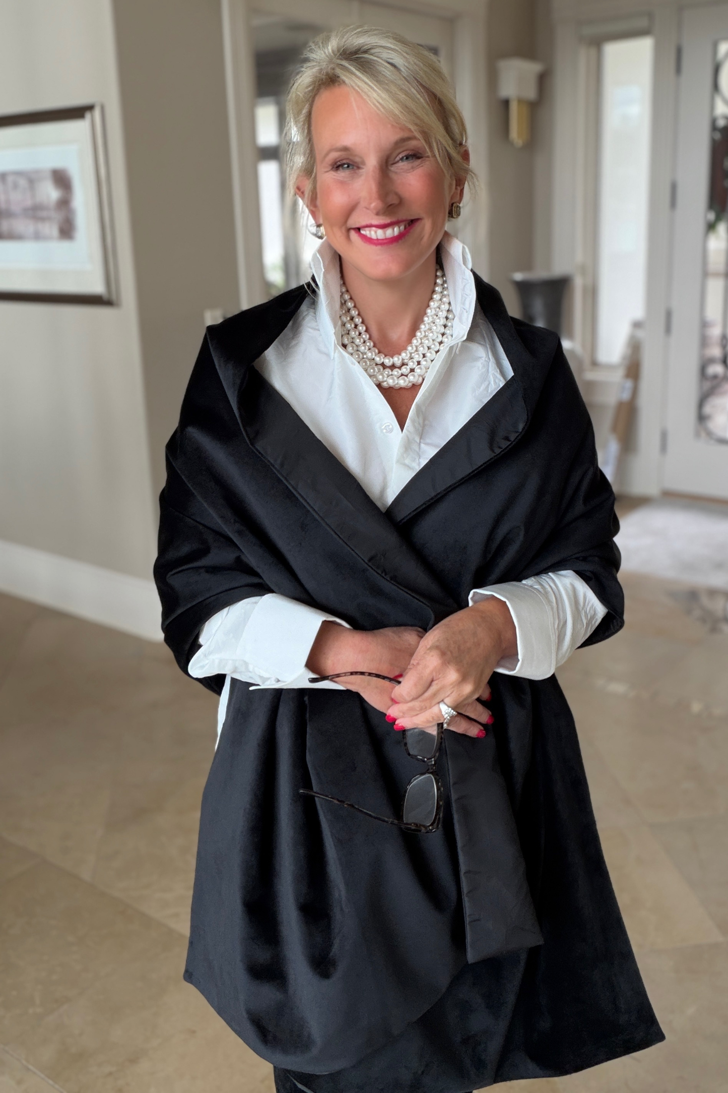 Midnight Wrap in black taffeta and velvet draped over a white blouse, styled with a layered pearl necklace in an elegant home hallway