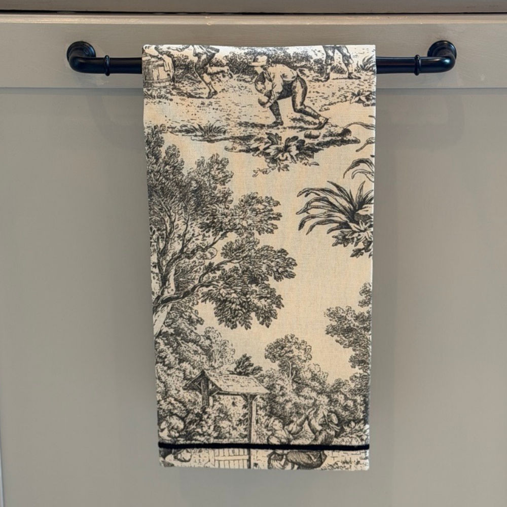 A cream with black Montefalco toile cotton towel hanging on a bar on a cabinet