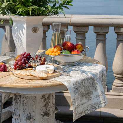 A table set with a charcuterie spread with a montefalco toile cotton runner in toile with a vase, wine and fruit