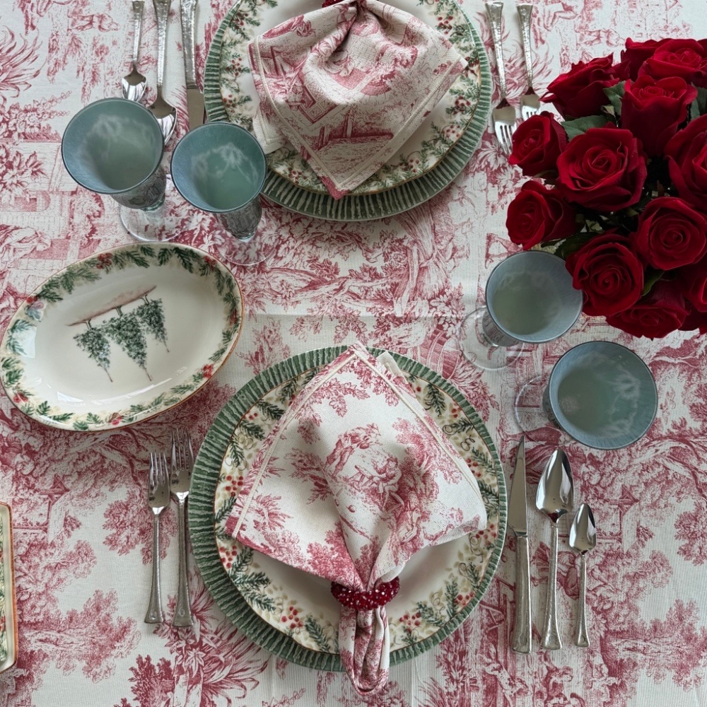 A table with a Montefalco tablecloth set with Natale plates and Montefalco Red cotton napkin with roses