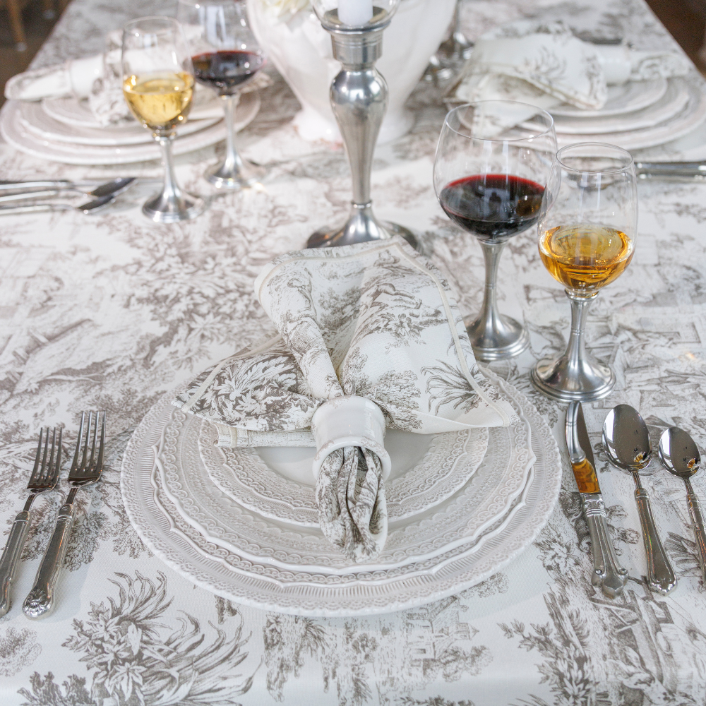Latte and Cream Montefalco Toile Cotton Napkin on a table with Plates, wineglasses and silverware, with a matching tablecloth by Arte Italica.