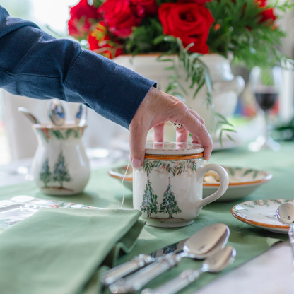A Natale Italian ceramic tea infuser mug being placed on a table with green linens and red roses