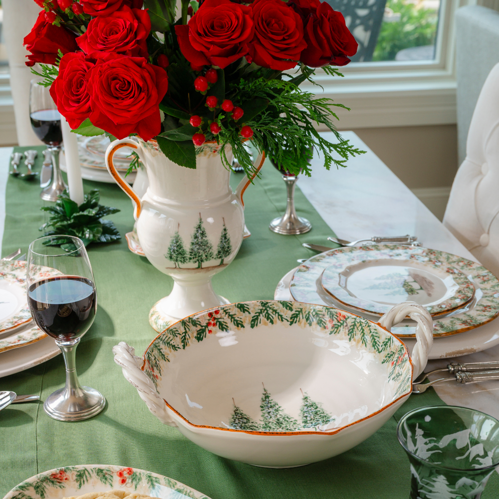 Natale ceramic twist handle bowl shown from the top with the Natale pine pattern around the edge and 3 hand painted pine trees on a table set with Natale and a Urn with red roses