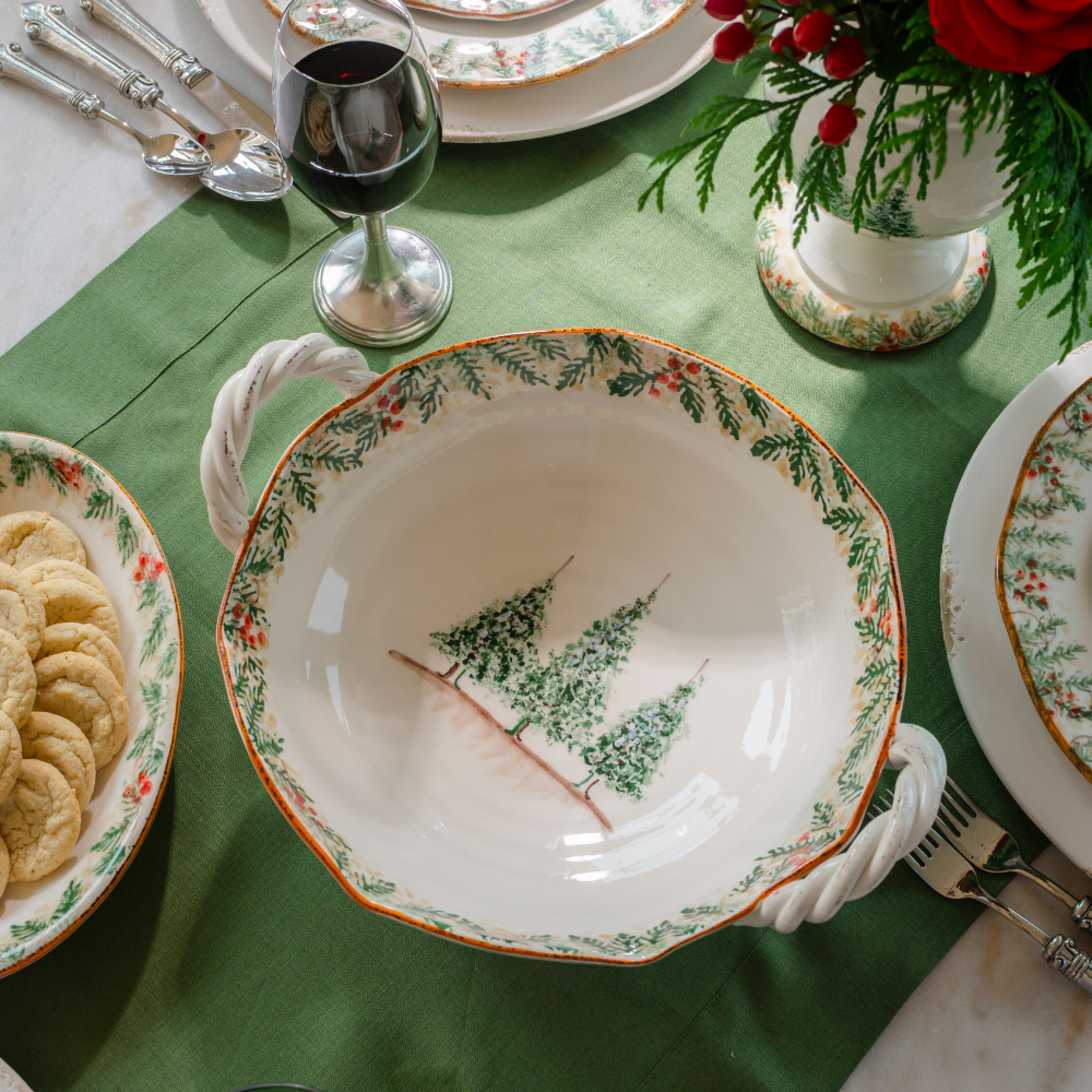 Natale ceramic twist handle bowl shown from the top with the Natale pine pattern around the edge and 3 hand painted pine trees in the middle on a evergreen linen runner on a table