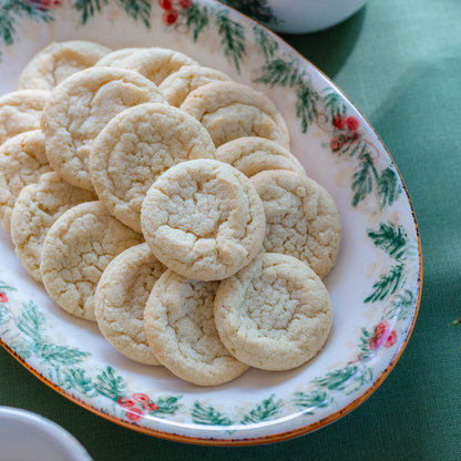 A close up of a Natale small ceramic oval dish with sugar cookies on it showing the hand painted detail around rim on a green background
