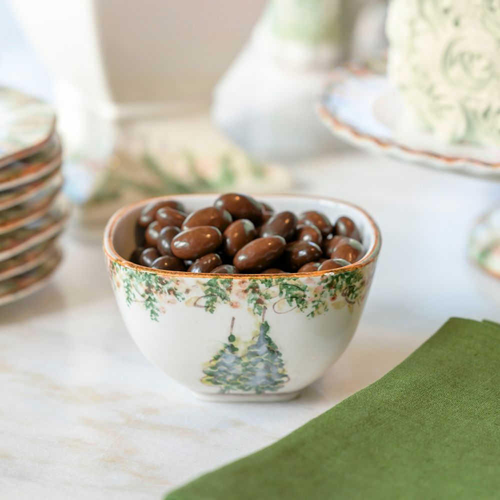 Close up of Natale Square Bowl with Chocolate covered Nuts on Table Arte Italica Natale small square bowl hand painted winterberries snowy trees Italian ceramic table service