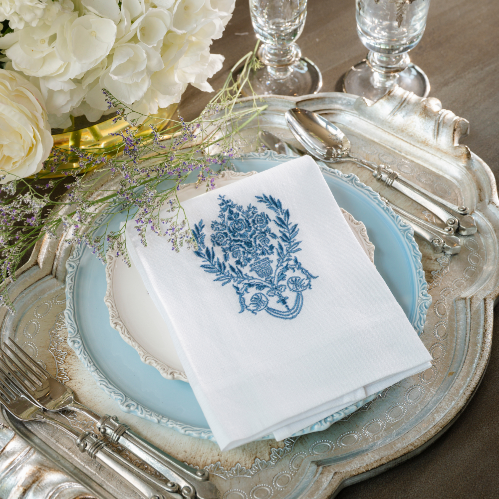 A white linen towel embroidered with a blue Nobel crest design folded on Imperial plates on a silver tray with flowers
