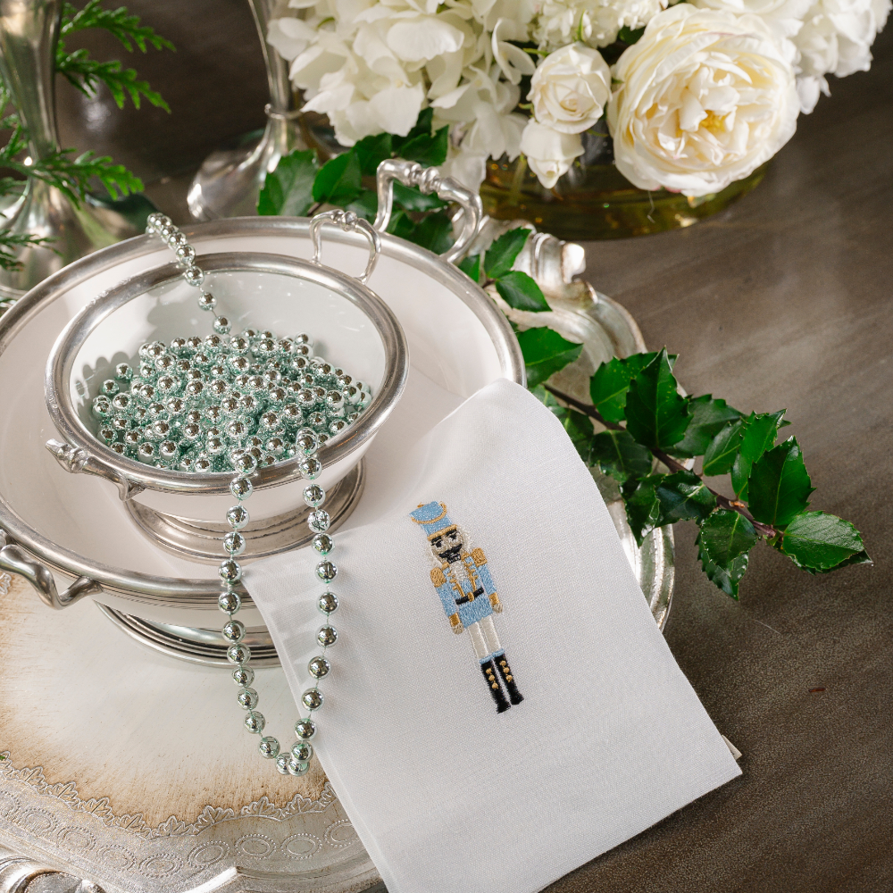 A white linen towel embroidered with a christmas nutcracker with a blue uniform on a Tuscan bowl with beads