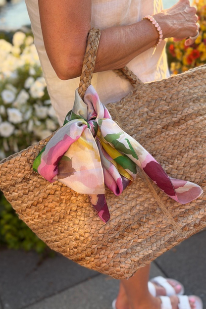 Woman holding a straw beach bag with a Portofino Summer garden silk scarf tied on the handle