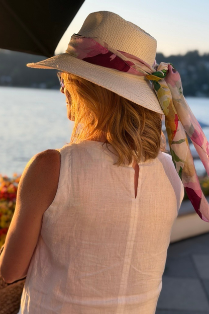 Woman wearing a hat on a patio with a Portofino summer garden silk scarf on it who is looking at the sunset