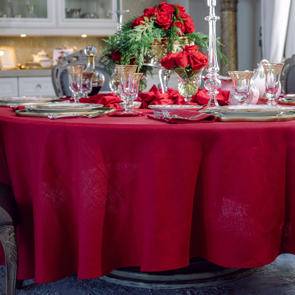 Decorated table with red linen tablecloth, napkins, and floral centerpieces in a kitchen setting.