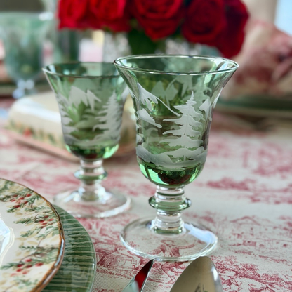 Two Rialto Winterscape etched pine design green glass Water and wine glass on a table with Natale and a red toile tablecloth
