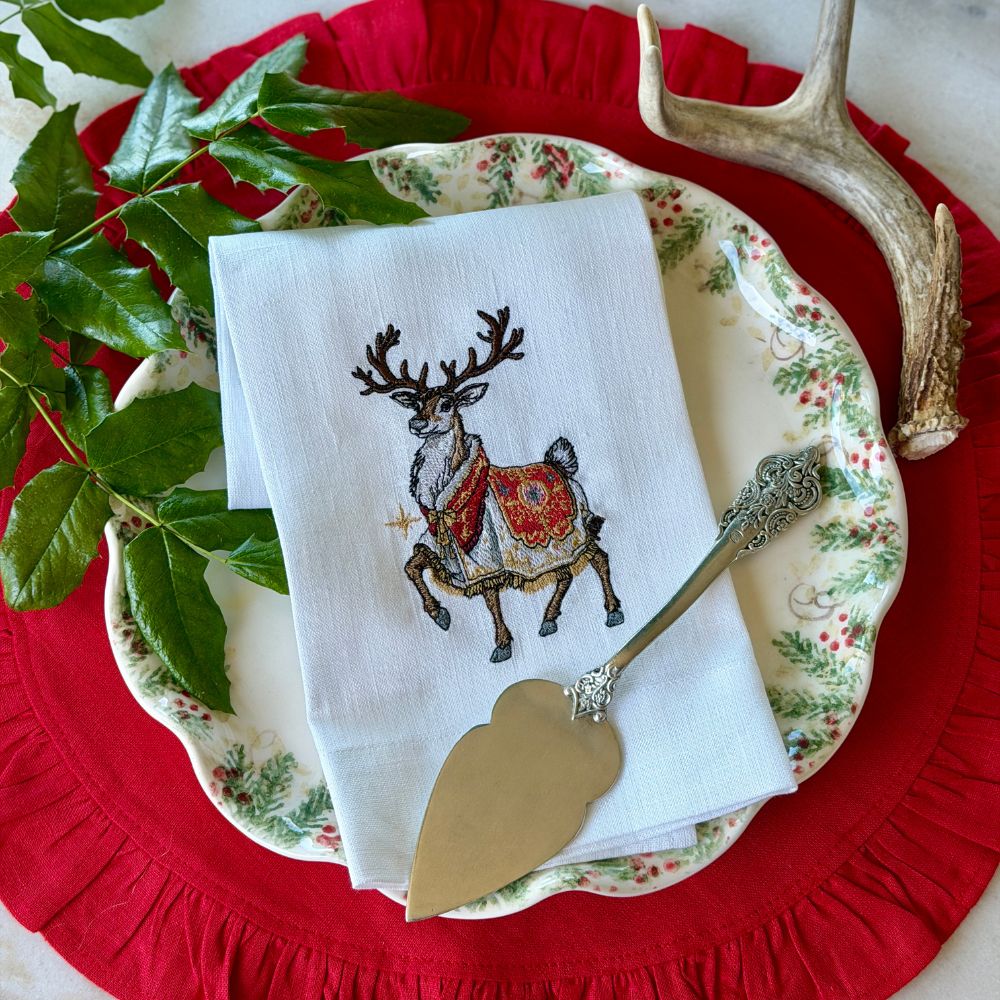Napkin with embroidered deer design on a Arte Italica Natale plate with a red Round Ruffle velvet placemat.