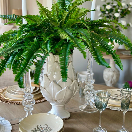 Decorative table setting with a large green fern in a Scavo Harvest artichoke shaped white vase, glasses, and plates.