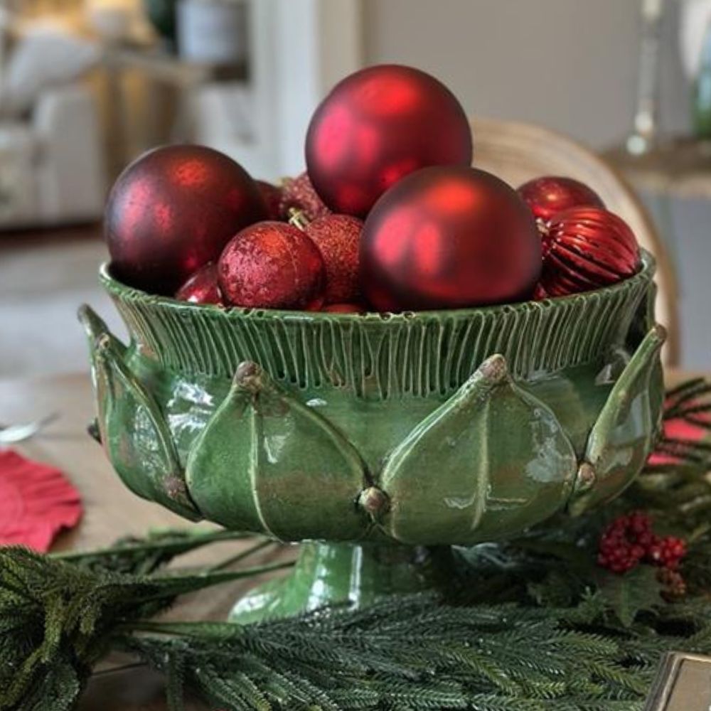 Italian Green artichoke inspired bowl filled with red ornaments on a table.