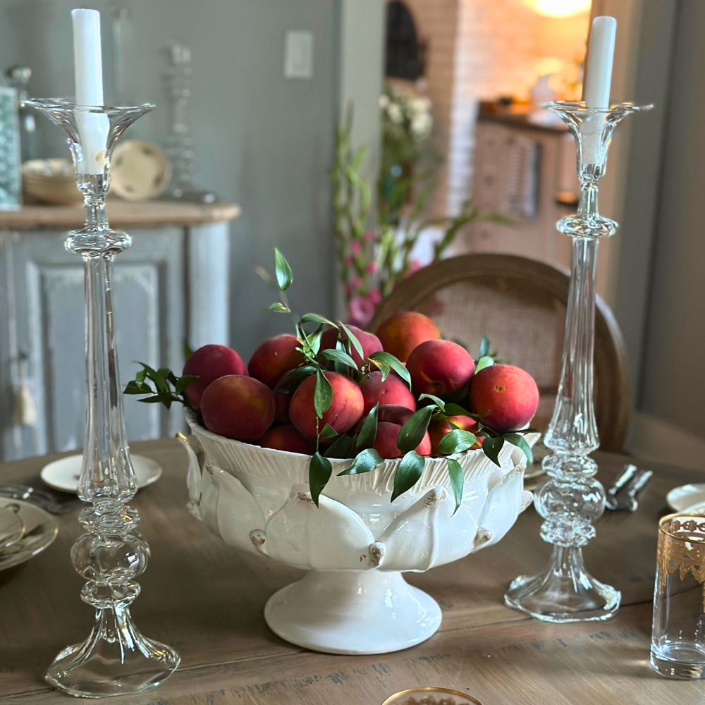 Scavo Harvest artichoke inspired Decorative bowl with peaches between two candlesticks on a table.