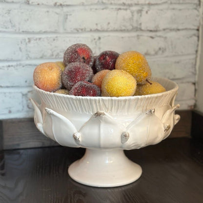 Decorative artichoke inspired white bowl with fruits on a wooden surface and brick wall background