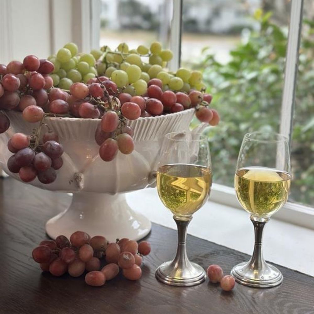 Scavo Harves Pedestal Bowl of grapes with two vetro wine glasses on a table near a window