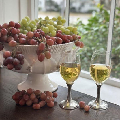 Scavo Harves Pedestal Bowl of grapes with two vetro wine glasses on a table near a window